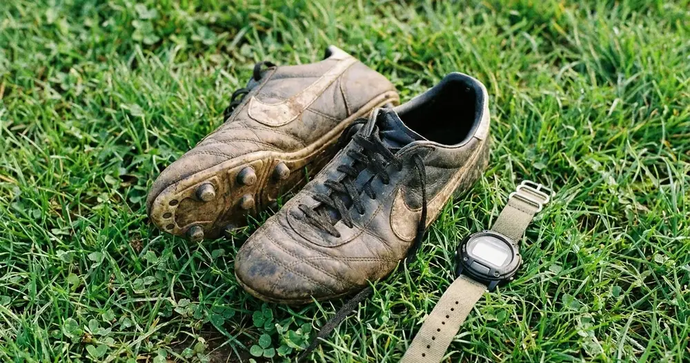 chuteiras e relógio esportivo sobre a grama de um campo